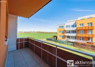 Balkon orientovaný na východ s výhledem na okolní zeleň a moderní bytovou zástavbu