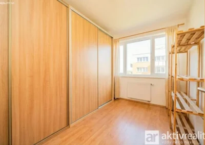 Samostatný pokoj využívaný jako šatna s velkými vestavěnými skříněmi a oknem v bytě 3+kk Praha Kyje