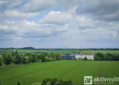 Výhled z terasy bytu na okolní zeleň, pole a panorama severní části Prahy.